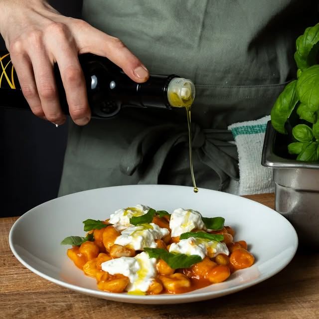 Olive oil poured over gnocchi with tomato, burrata and basil